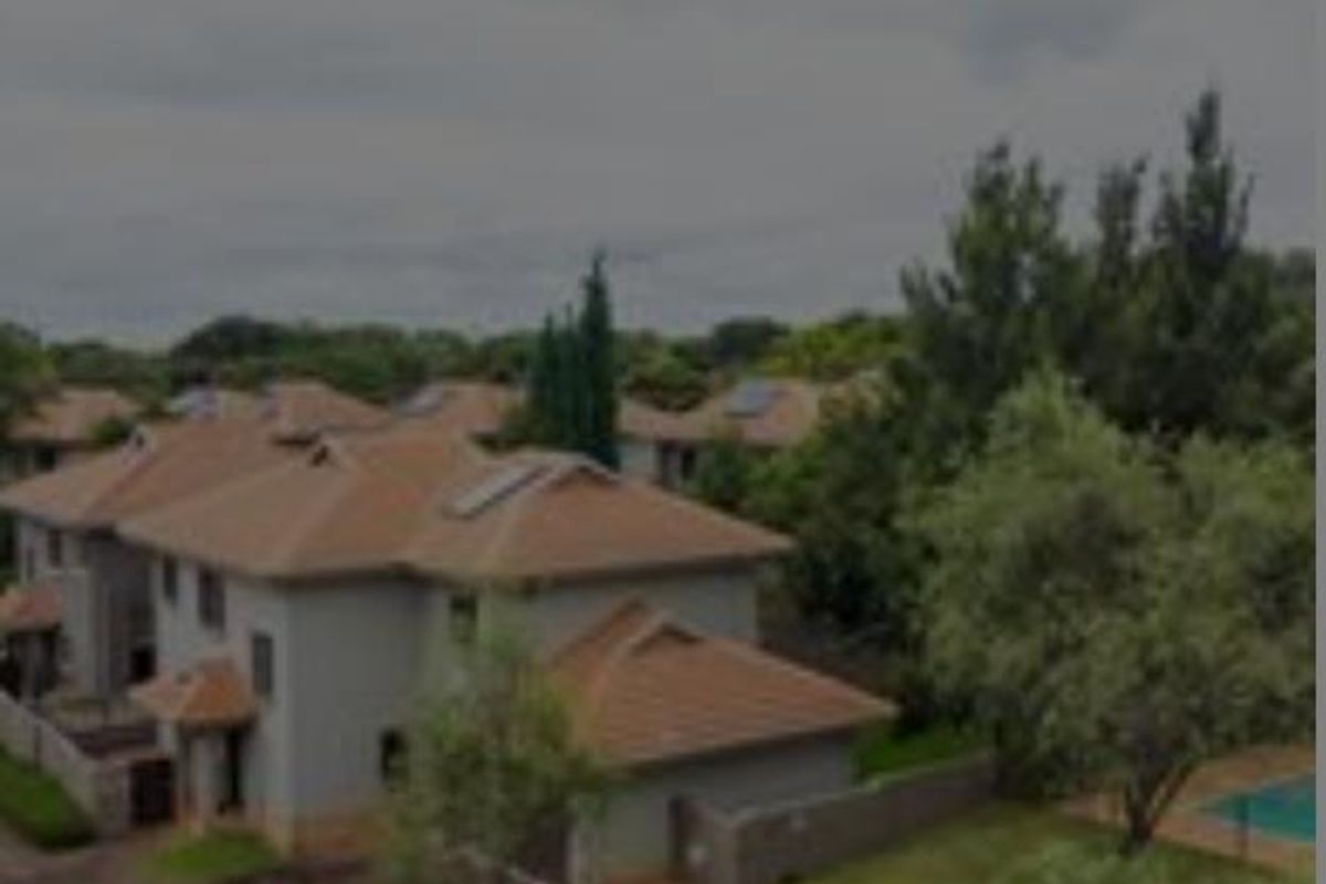 Aerial view of a residential apartment complex featuring tiled roofs, solar panels, communal garden areas, and a swimming pool.