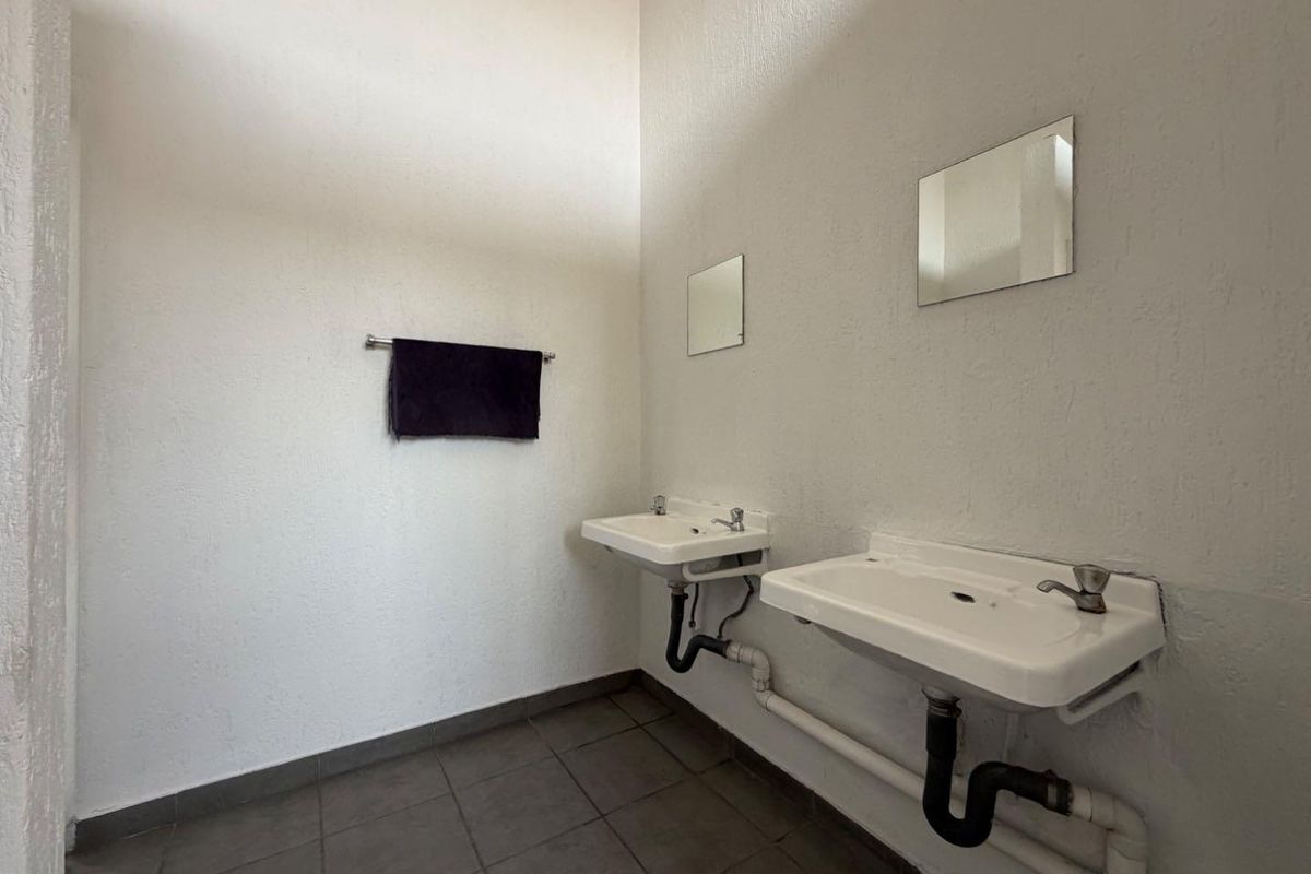 A functional bathroom space featuring dual wall-mounted ceramic basins with exposed plumbing and tiled flooring, offering a blank canvas for renovation.