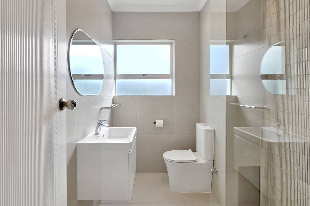 Modern, well-maintained bathroom featuring a wall-mounted vanity, sleek basin, toilet, and a glass-enclosed shower with neutral floor-to-ceiling tiling.