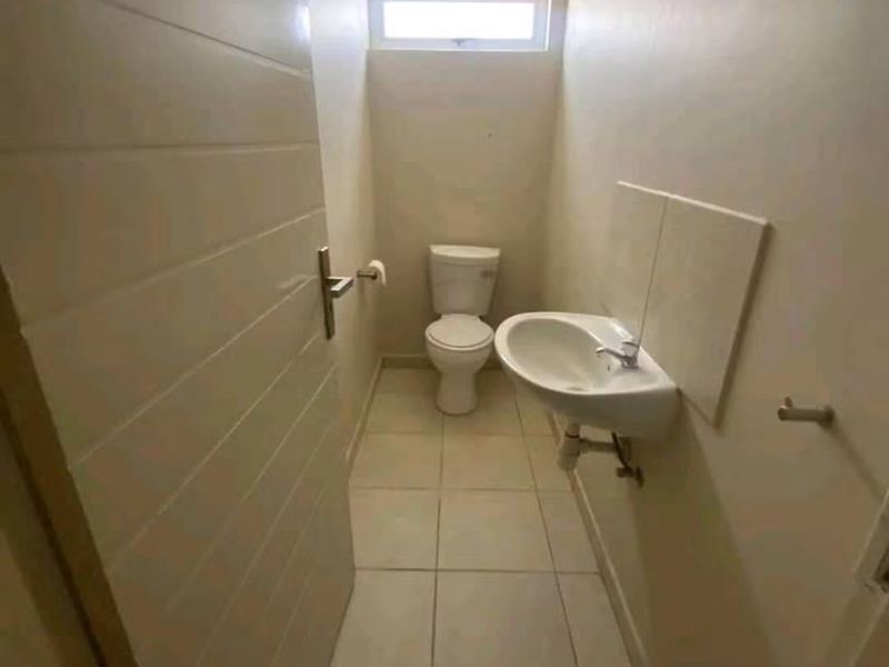 A compact guest bathroom featuring a wall-mounted basin, toilet, tiled flooring, and a high-set clerestory window for natural light.