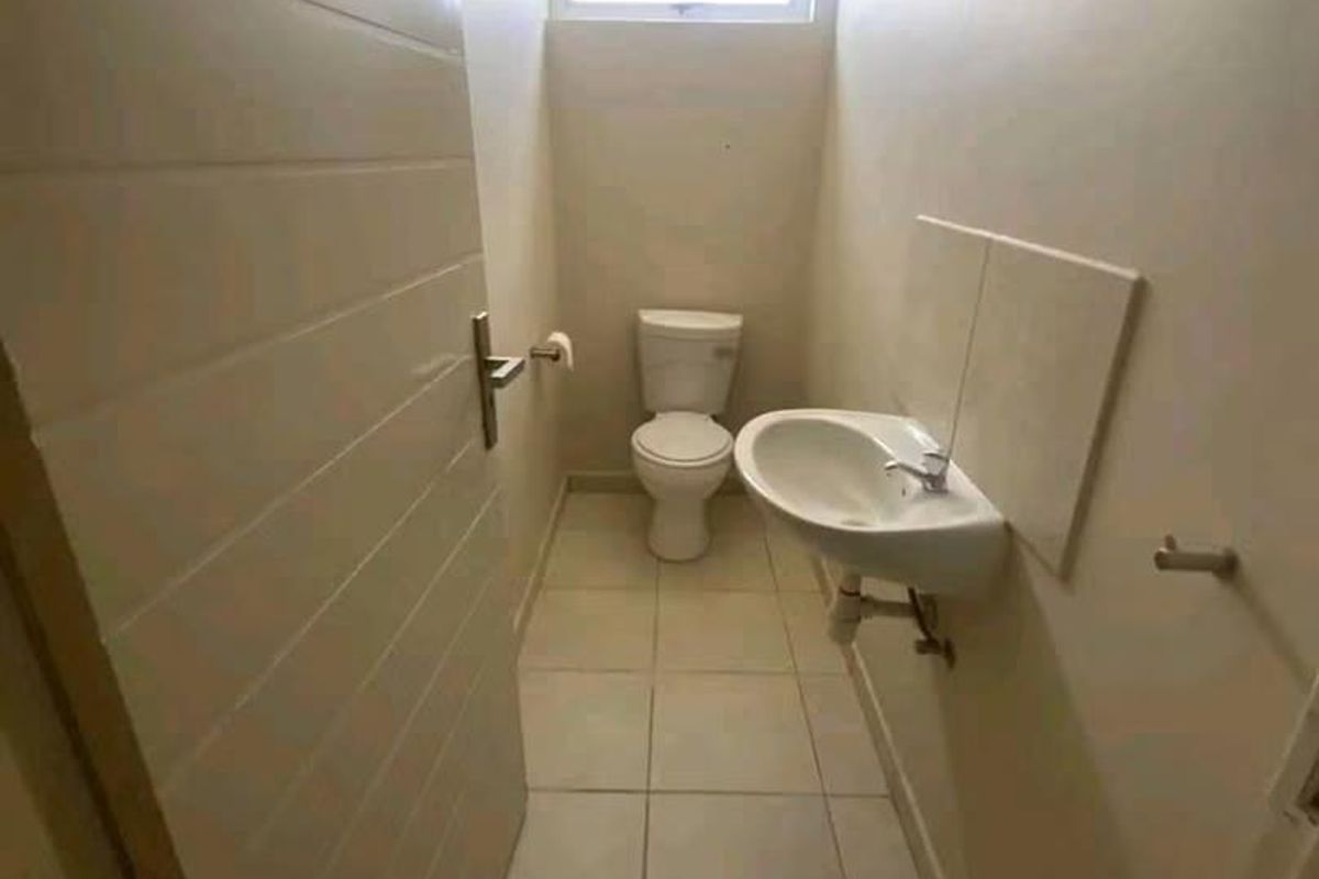 A compact guest bathroom featuring a wall-mounted basin, toilet, tiled flooring, and a high-set clerestory window for natural light.