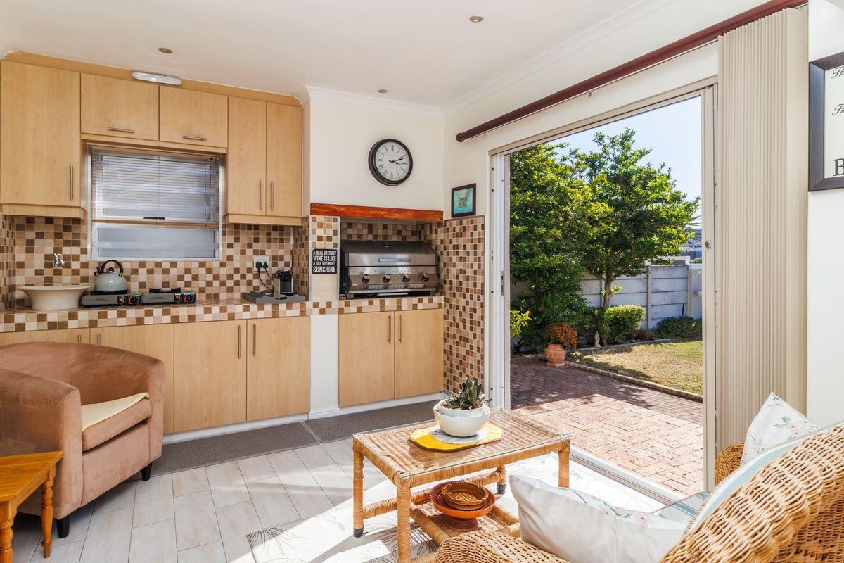 A functional kitchen area featuring light wood cabinetry, tiled backsplash, and a built-in braai, with direct access to the rear garden through sliding doors.