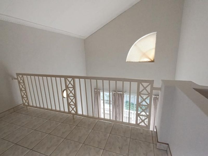 An open mezzanine landing area featuring tiled flooring, a decorative metal balustrade, and a vaulted ceiling with an arched window.