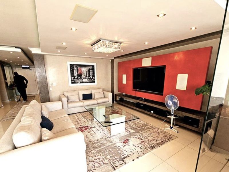 Spacious living room featuring a prominent red built-in media wall, recessed ceiling lighting, integrated speakers, and polished tiled flooring.