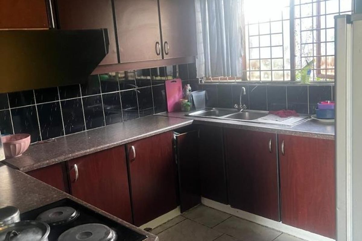 Functional kitchen featuring dark laminate cabinetry, contrasting countertops, a double bowl sink, and a built-in electric hob with an extractor fan.