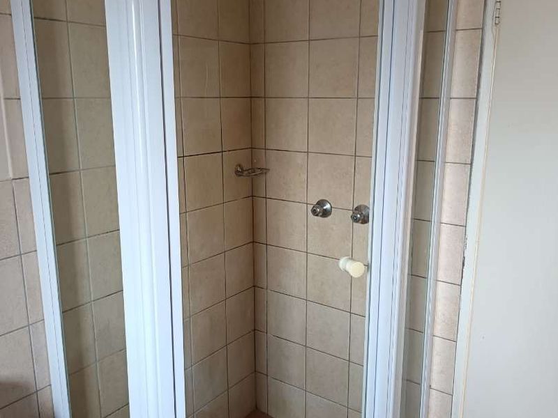 A functional corner shower unit with white frame, tiled walls, and tiled flooring in a standard bathroom setting.