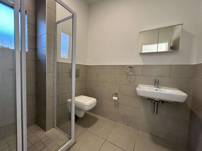 A functional bathroom featuring a wall-mounted toilet, a glass shower enclosure, and a wall-mounted basin with a medicine cabinet.