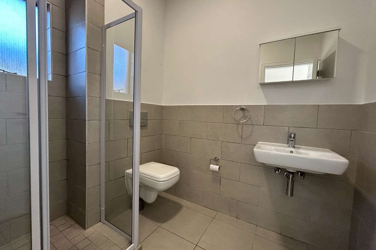 A functional bathroom featuring a wall-mounted toilet, a glass shower enclosure, and a wall-mounted basin with a medicine cabinet.