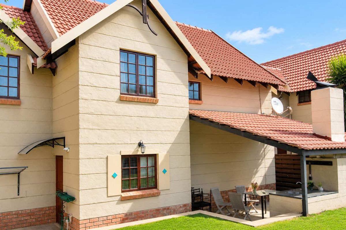 Rear view of the townhouse featuring a covered patio with a built-in braai, outdoor sink, and access to a private garden area.