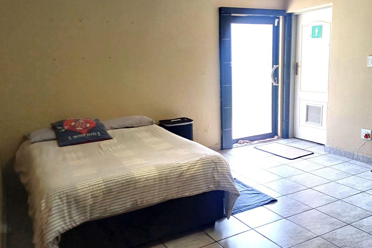 A bedroom featuring tiled flooring, a sliding glass door providing natural light, and an internal door, with walls showing signs of wear.