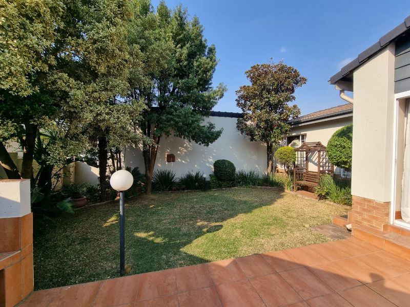 A private rear garden featuring a tiled patio area, established trees, and a perimeter wall, providing a pleasant outdoor space for the townhouse.