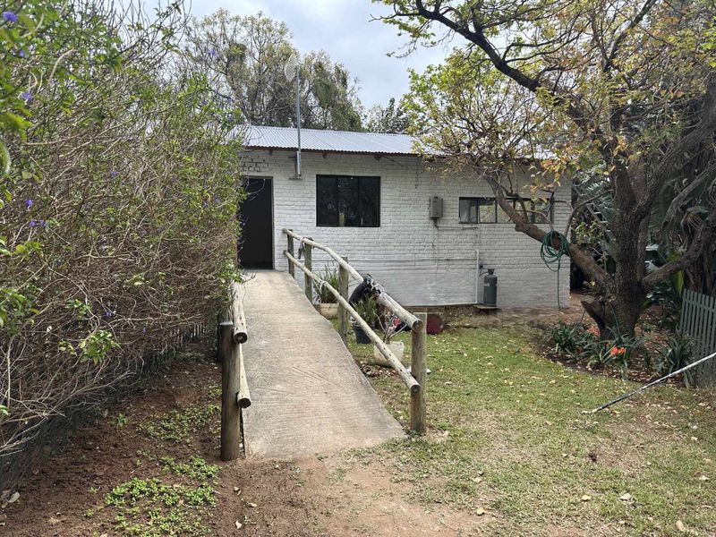 Rear view of a detached structure featuring a painted brick facade, corrugated metal roof, and a concrete access ramp with timber handrails.