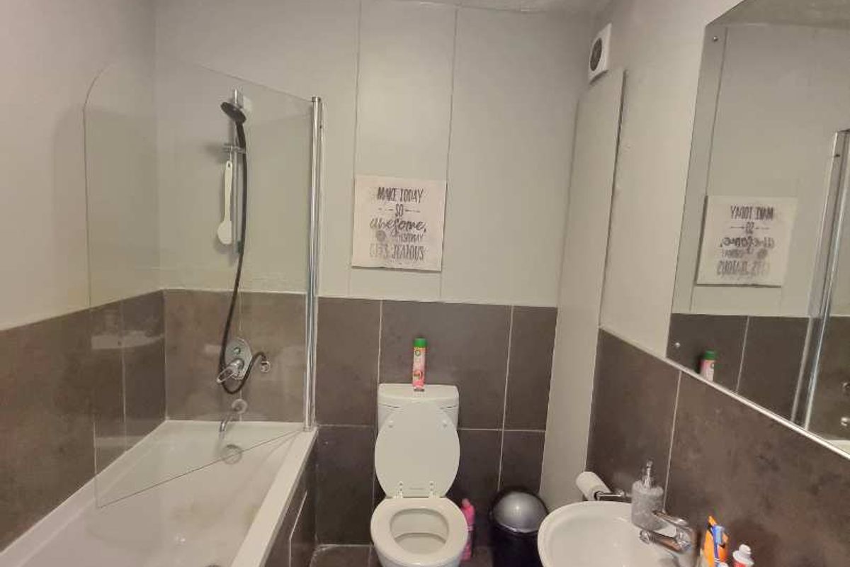 A functional bathroom featuring a bathtub with a glass shower screen, a pedestal sink, and a toilet, finished with neutral wall and floor tiling.