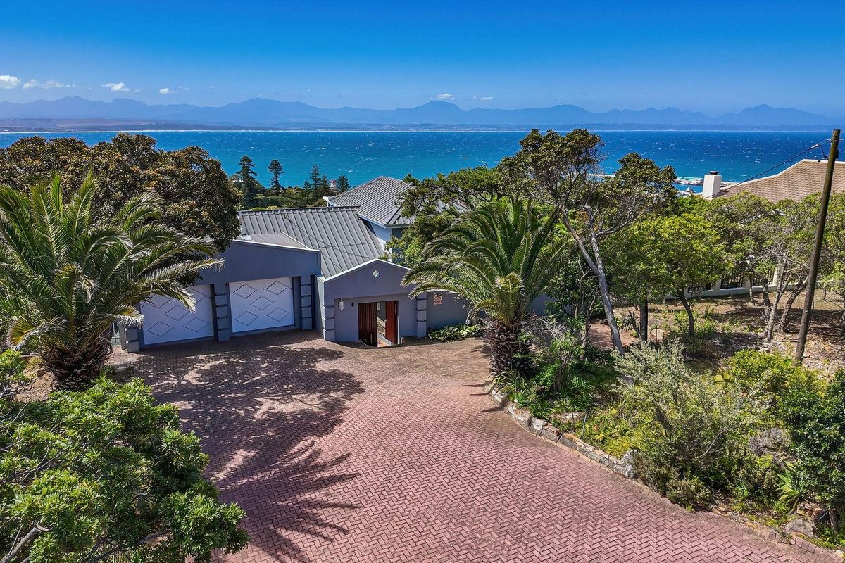 Aerial view of the property featuring a paved driveway, double garage, and landscaped garden with a scenic ocean and mountain backdrop.