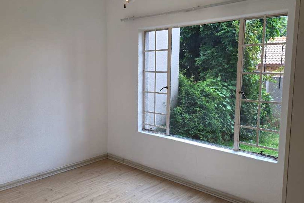 A bright, empty bedroom featuring light wood-look flooring, a ceiling fan, and a large window overlooking the garden.