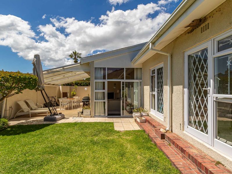 Rear exterior view featuring a paved covered patio, brick step transition, and sliding glass doors leading into the home, set against a landscaped lawn.