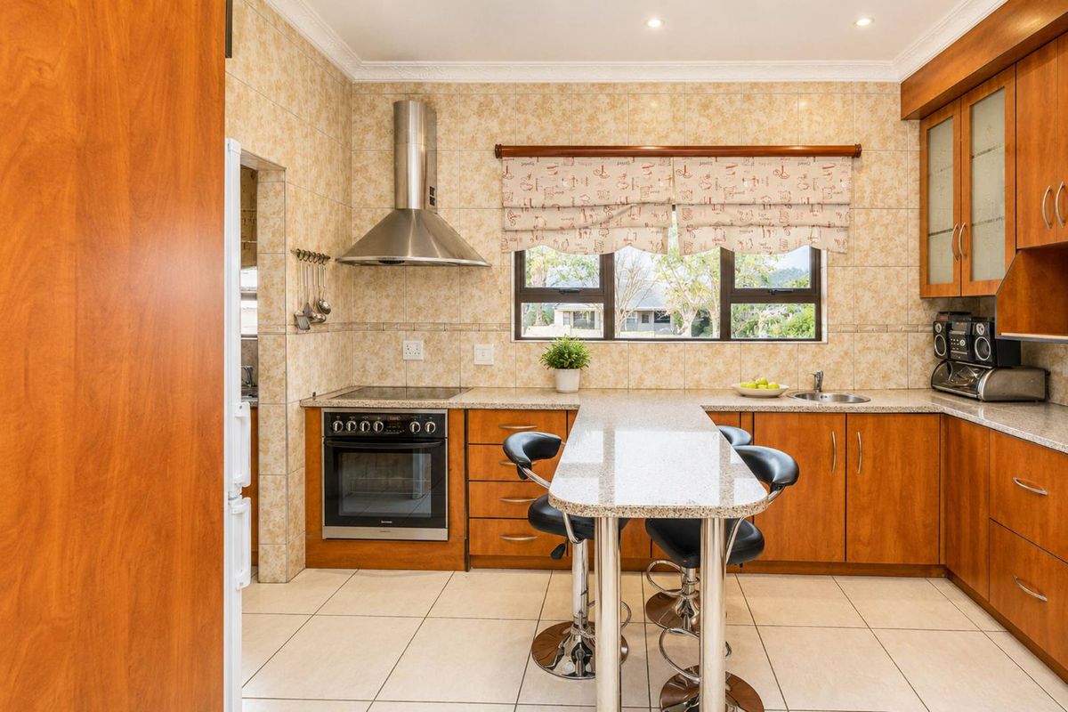 A functional kitchen featuring warm-toned wooden cabinetry, granite countertops, a built-in oven with extractor fan, and a convenient breakfast bar area.