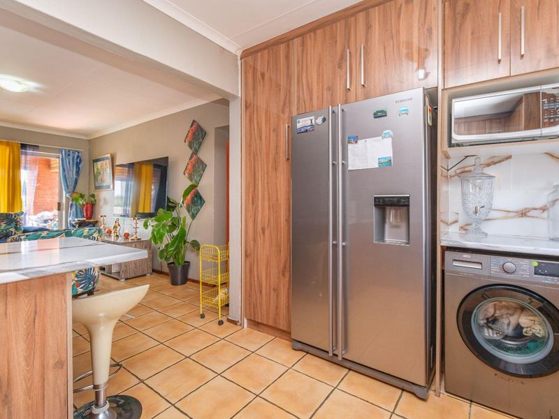 Open plan kitchen and living area featuring wood-look cabinetry, tiled flooring, and integrated appliance housing.