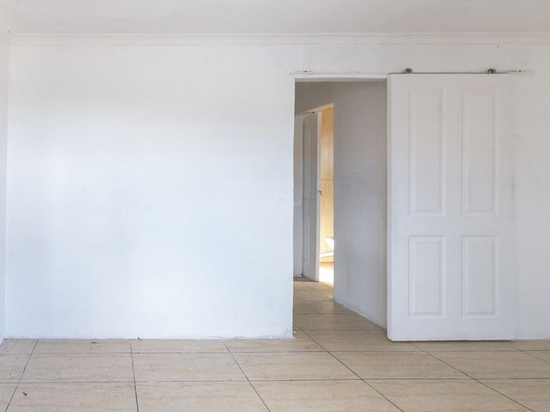 An empty living area featuring tiled flooring, a sliding door, and a timber entrance door, offering a blank canvas for renovation.