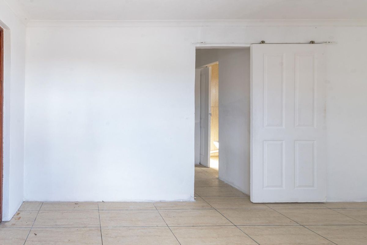 An empty living area featuring tiled flooring, a sliding door, and a timber entrance door, offering a blank canvas for renovation.