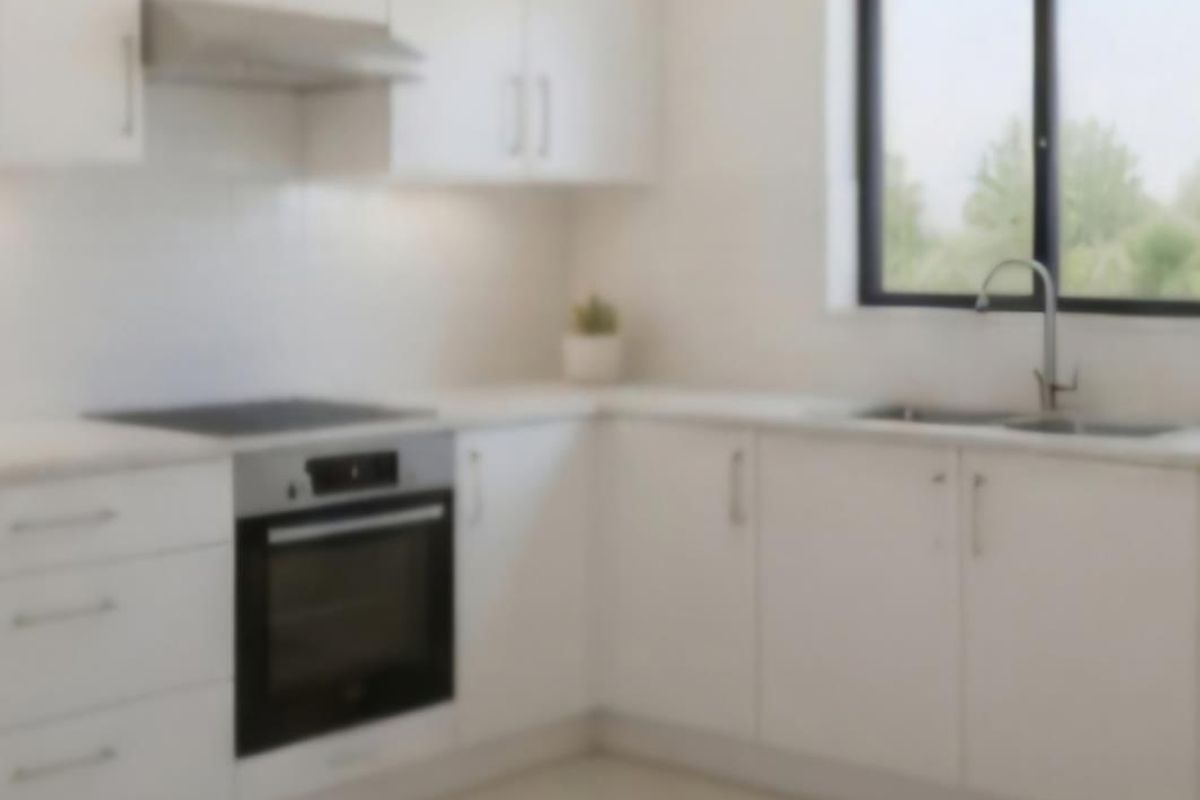 A modern, minimalist kitchen featuring white cabinetry, stone countertops, integrated oven, electric cooktop, and a double bowl sink with a view through the window.
