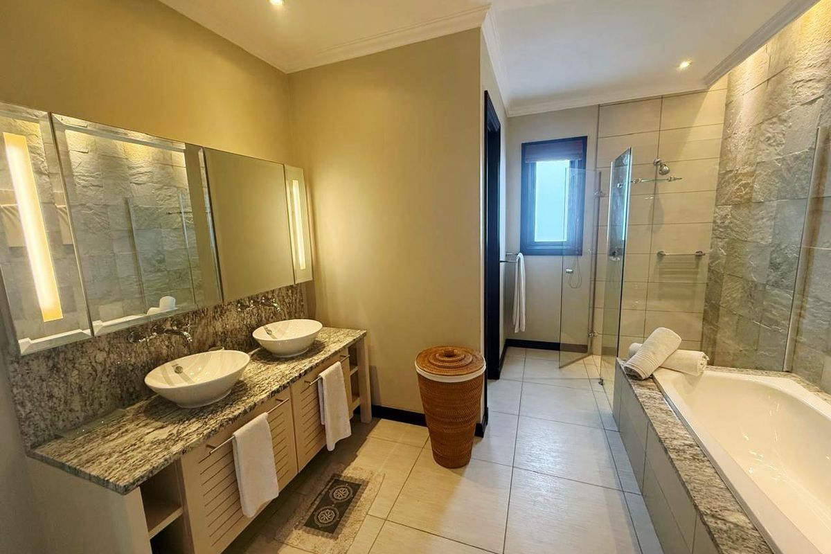 A well-appointed bathroom featuring a double vanity with granite countertops, vessel sinks, a glass-enclosed shower, and a separate bathtub with stone tile accents.