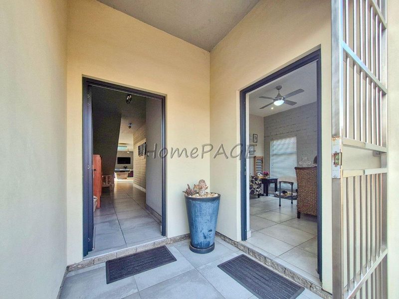 A covered patio area featuring tiled flooring and a metal security gate, providing access to the interior living spaces.