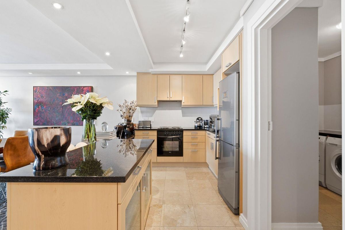 Modern kitchen featuring light wood cabinetry, granite countertops, integrated appliances, and recessed lighting, seamlessly flowing into the adjacent living area.