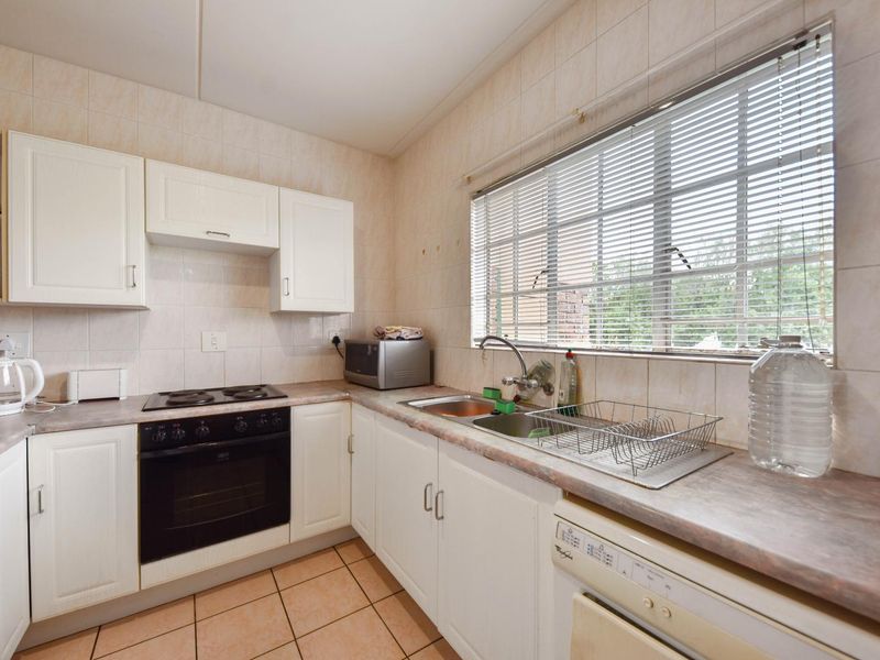 A functional kitchen featuring white cabinetry, laminate countertops, an integrated electric oven and hob, and a stainless steel double sink with tiled splashbacks.