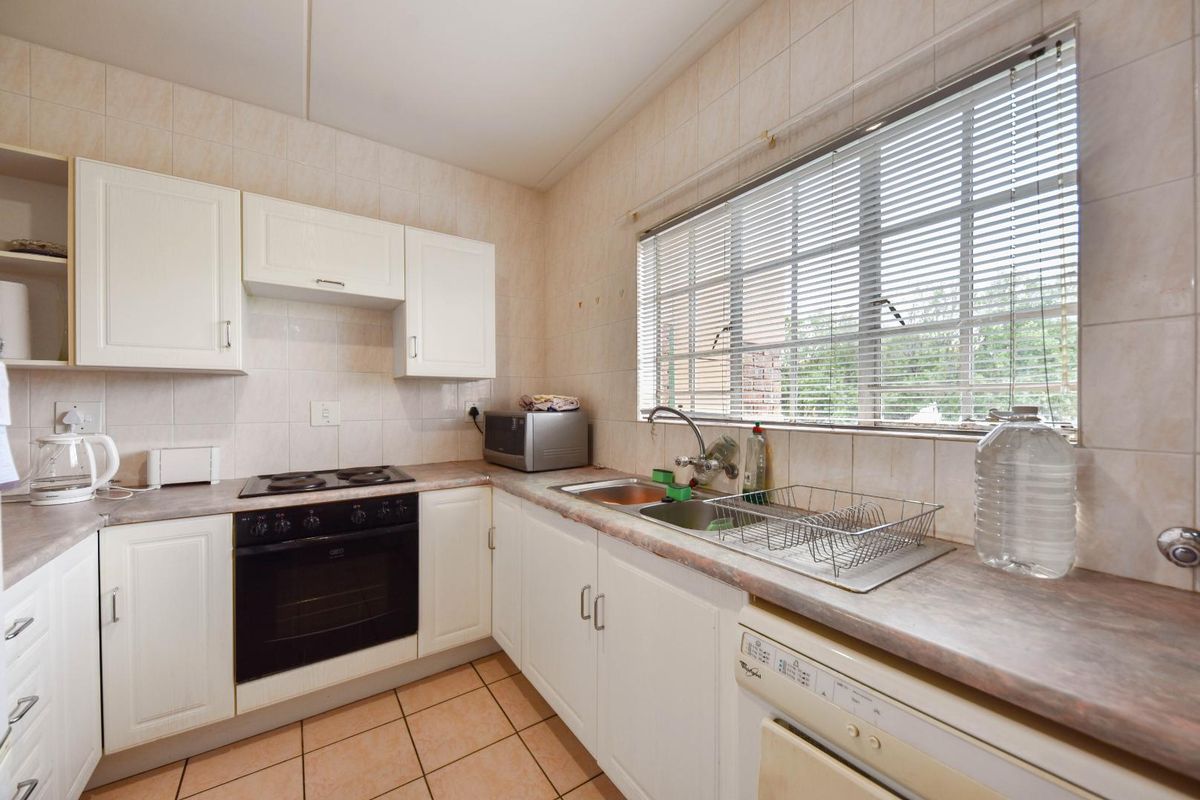 A functional kitchen featuring white cabinetry, laminate countertops, an integrated electric oven and hob, and a stainless steel double sink with tiled splashbacks.