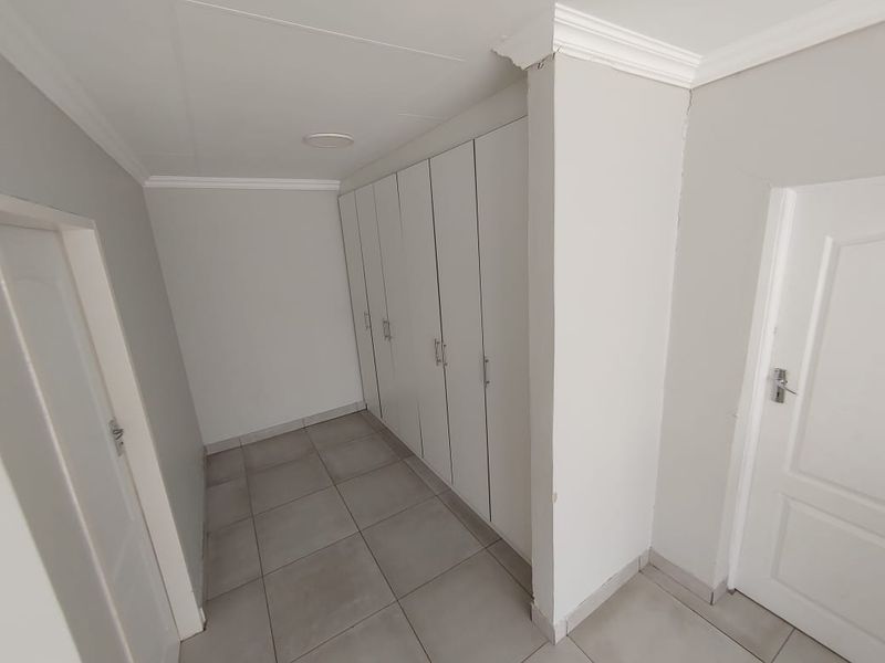 A clean, empty hallway featuring neutral tiled flooring and extensive built-in cupboard storage with white cabinetry.