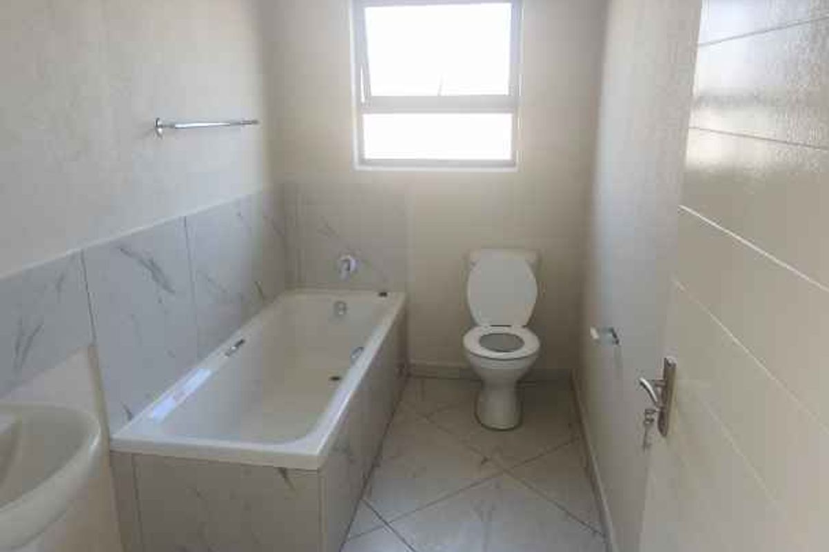 A clean, functional bathroom featuring a bathtub, pedestal basin, and toilet with neutral floor and wall tiling.