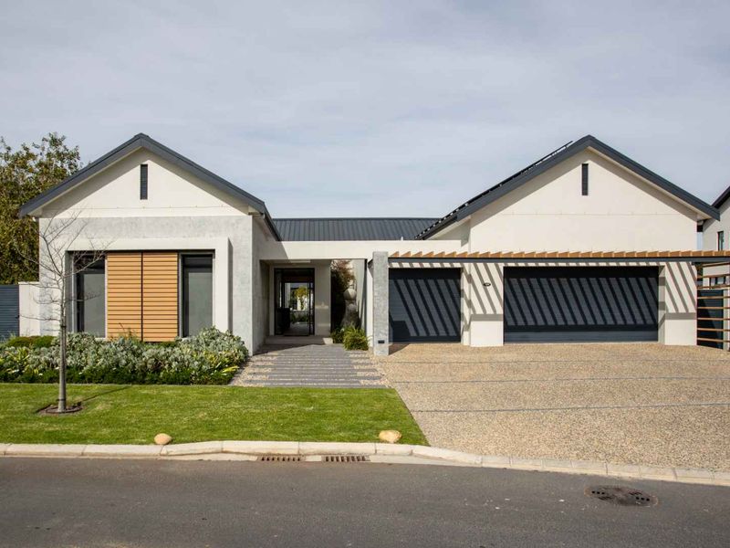 Modern single-story residence featuring a double garage, timber pergola, paved driveway, and well-maintained landscaped garden with contemporary architectural finishes.