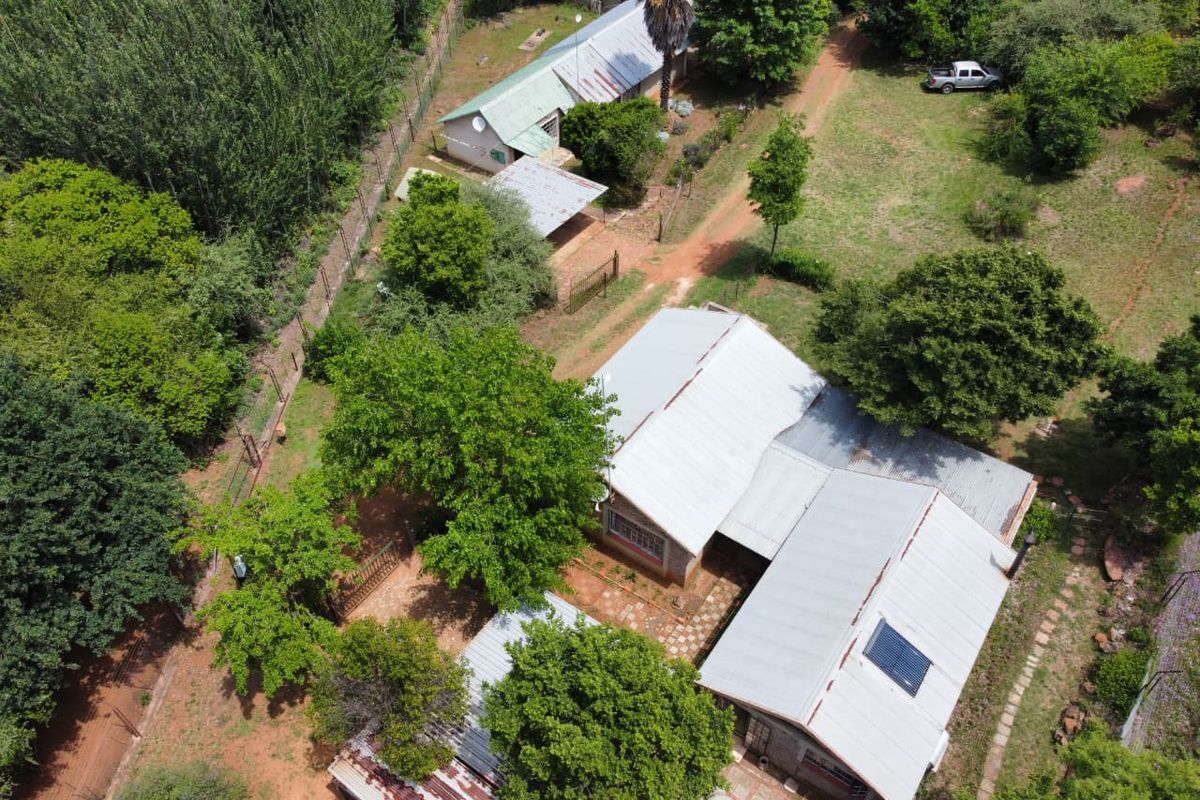 Aerial view of a rural property featuring a main residence with metal roofing, solar water heating, and multiple outbuildings set within a large garden.