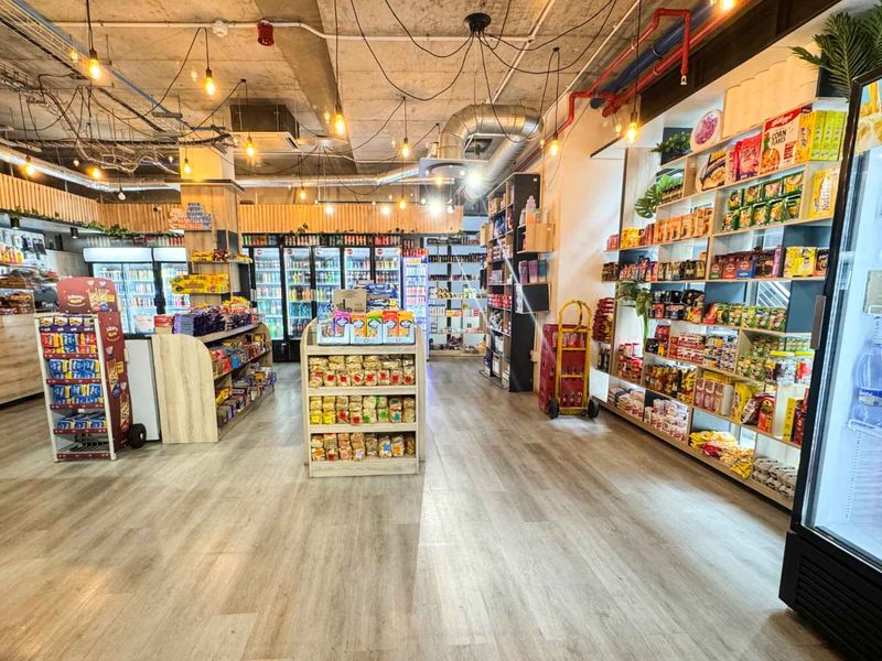 A modern retail space featuring an open-plan layout with exposed industrial ceilings, laminate flooring, and extensive built-in shelving and commercial refrigeration units.