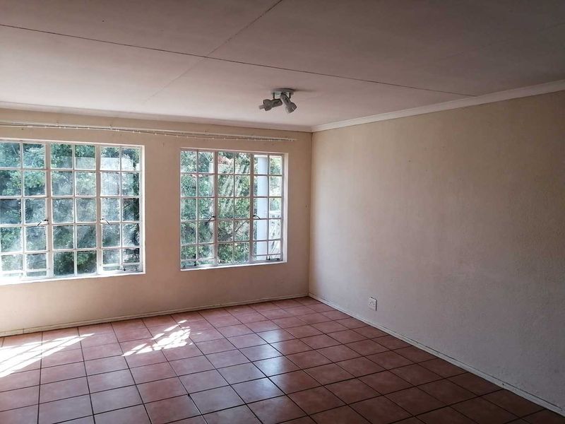 An empty living room featuring tiled flooring, large multi-pane windows providing natural light, and a ceiling-mounted spotlight fixture.