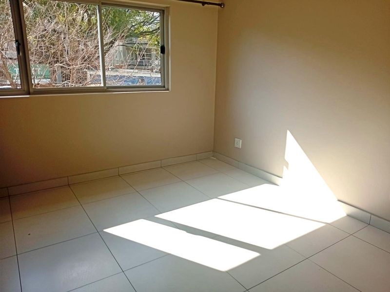 A bright, empty bedroom featuring neutral walls, tiled flooring, and a large sliding window that allows for ample natural light.