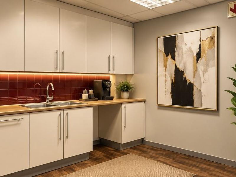 A modern office kitchenette featuring sleek white cabinetry, a wood-look countertop, a tiled backsplash, and a professional glass-partitioned entrance.