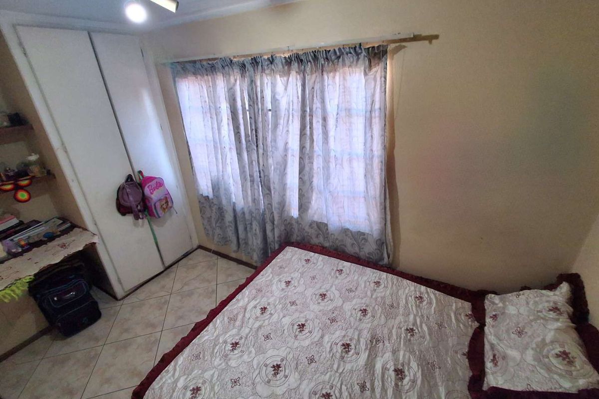 A bedroom featuring tiled flooring, a built-in wardrobe, and a ceiling fan, currently showing signs of wear on the wall finishes.