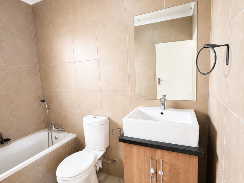 A clean, functional bathroom featuring neutral wall tiles, a modern vanity with a vessel basin, a built-in bathtub, and a wall-mounted mirror.