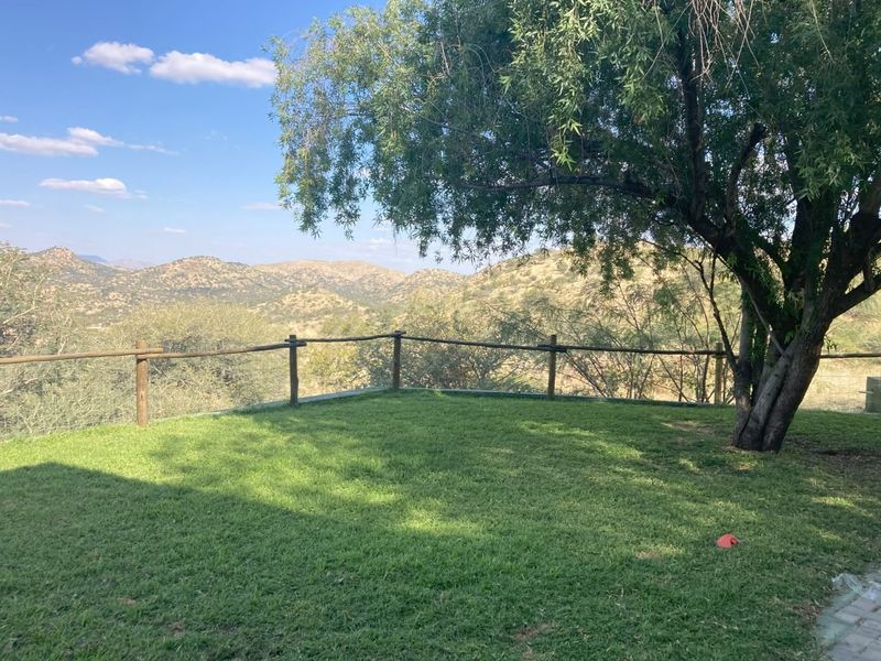 A well-maintained garden area featuring a lawn, mature tree, and a wooden fence, offering expansive scenic views of the surrounding hills.