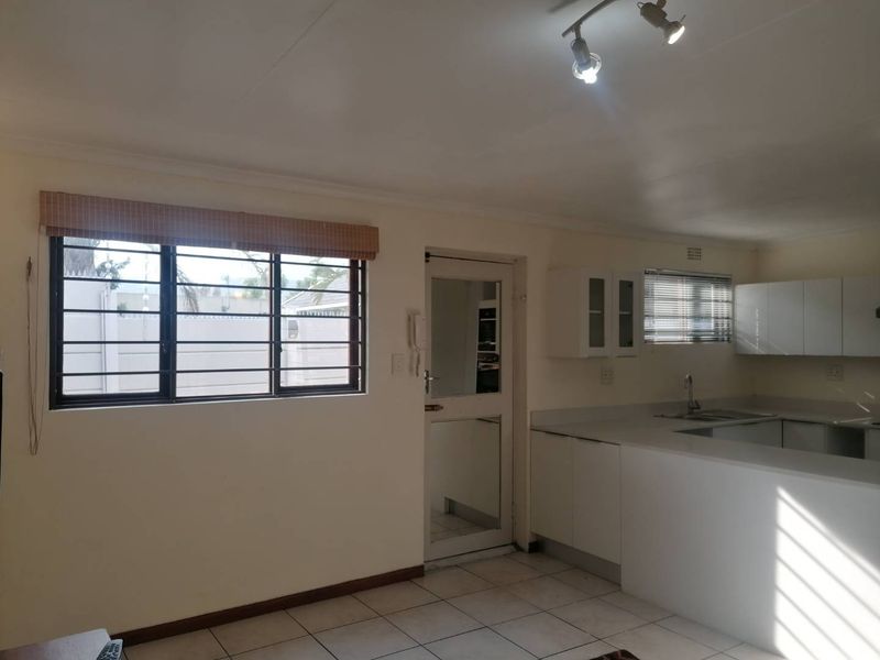 Open plan living and kitchen area featuring tiled flooring, security bars on windows, and functional built-in cabinetry.