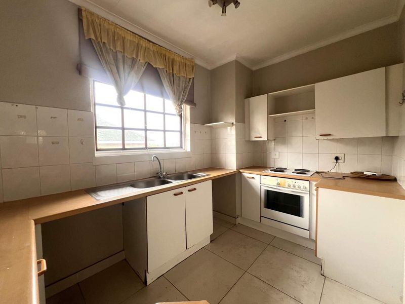 A functional kitchen featuring built-in cabinetry, laminate countertops, a double basin sink, and an integrated electric oven and hob with tiled splashbacks.