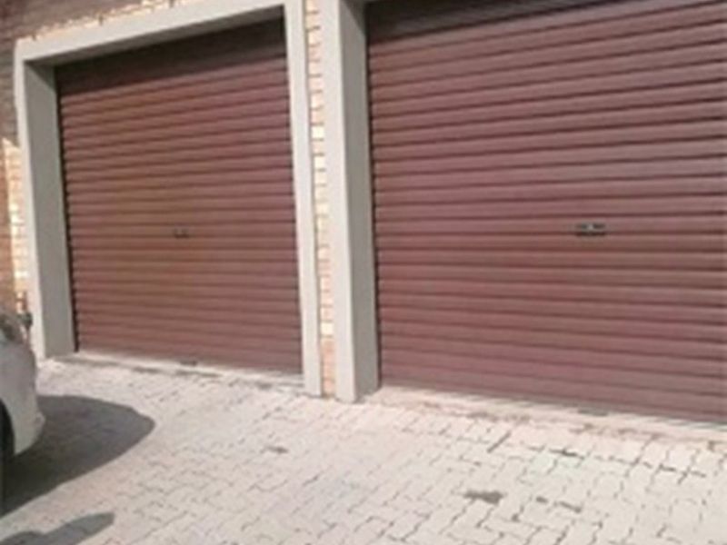 A double garage featuring brown roller doors and a paved driveway, set against a brick exterior wall.