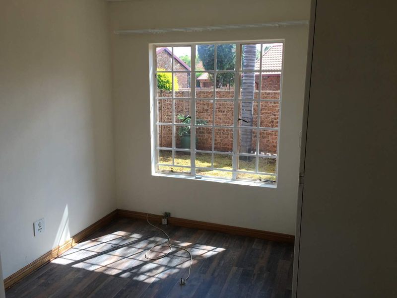 A bright, empty bedroom featuring laminate flooring, a built-in cupboard, and a large grid-pane window overlooking the rear garden area.