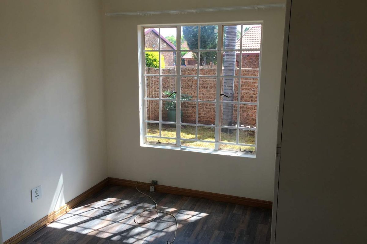 A bright, empty bedroom featuring laminate flooring, a built-in cupboard, and a large grid-pane window overlooking the rear garden area.