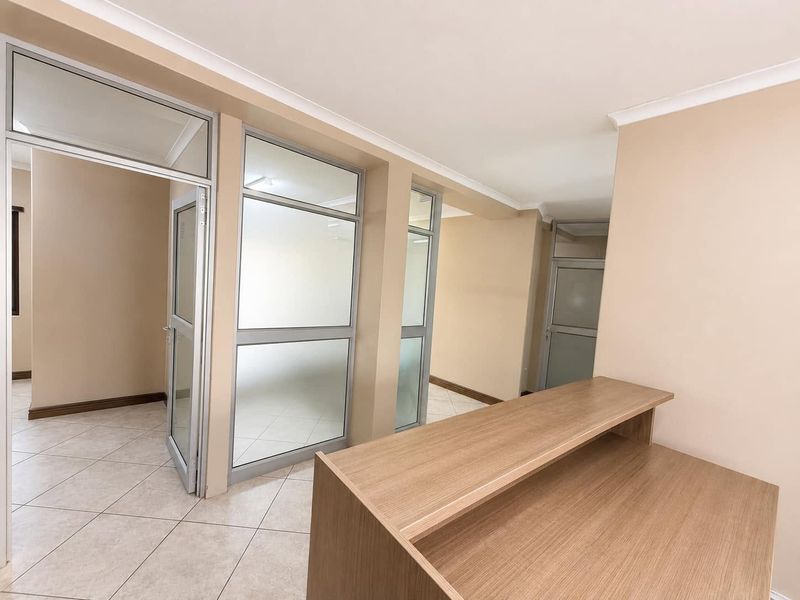A bright, modern office space featuring tiled flooring, aluminium-framed glass partitions, and a built-in reception counter.