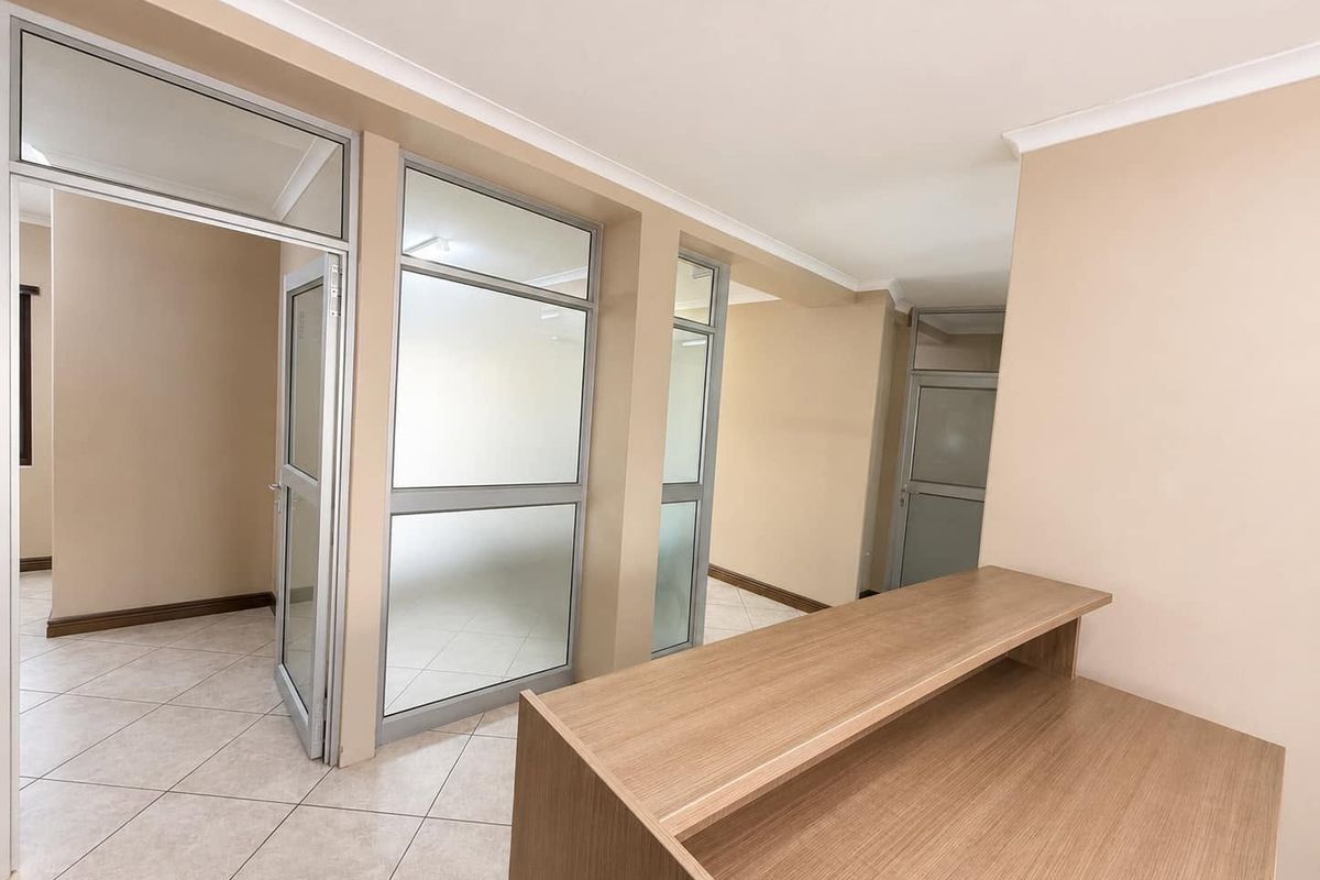 A bright, modern office space featuring tiled flooring, aluminium-framed glass partitions, and a built-in reception counter.