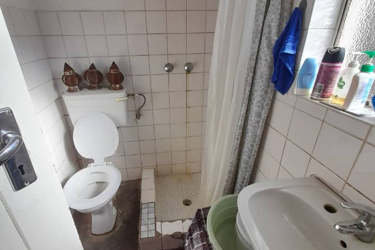 A compact bathroom featuring a shower area, toilet, and wall-mounted basin with dated tiling and visible signs of wear on fixtures.