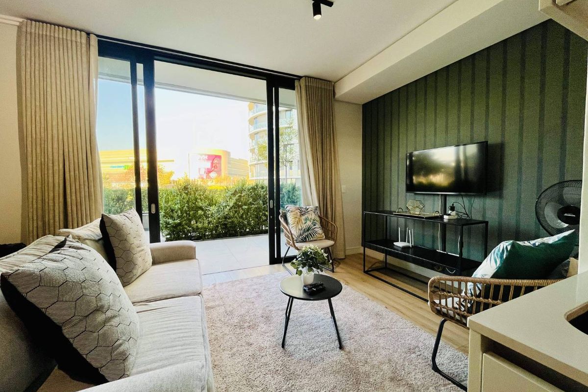 Modern living room featuring large sliding glass doors leading to a private balcony, complemented by a stylish accent wall and track lighting.